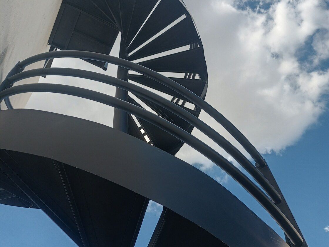 Escalera de caracol metálica de doble altura vista desde abajo contra el cielo