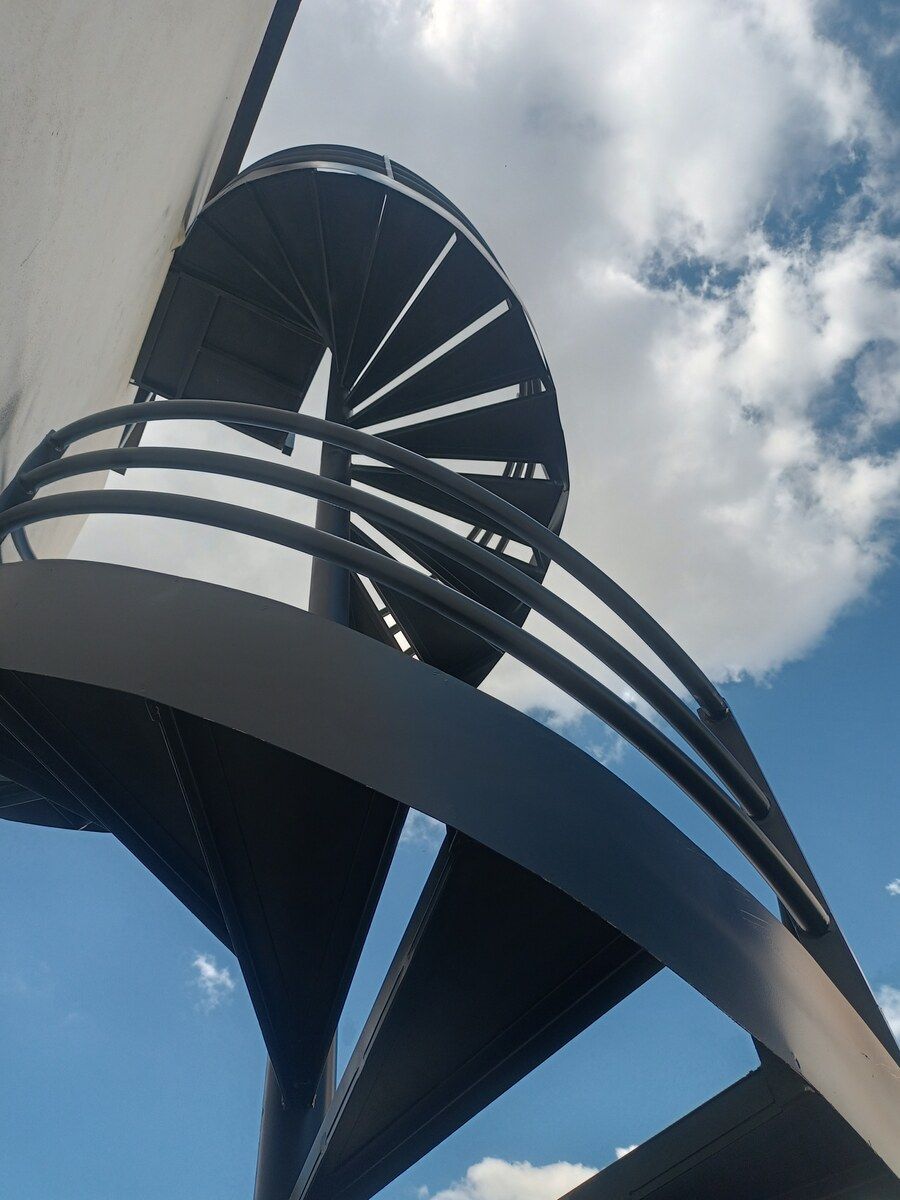 Escalera de caracol metálica de doble altura vista desde abajo contra el cielo